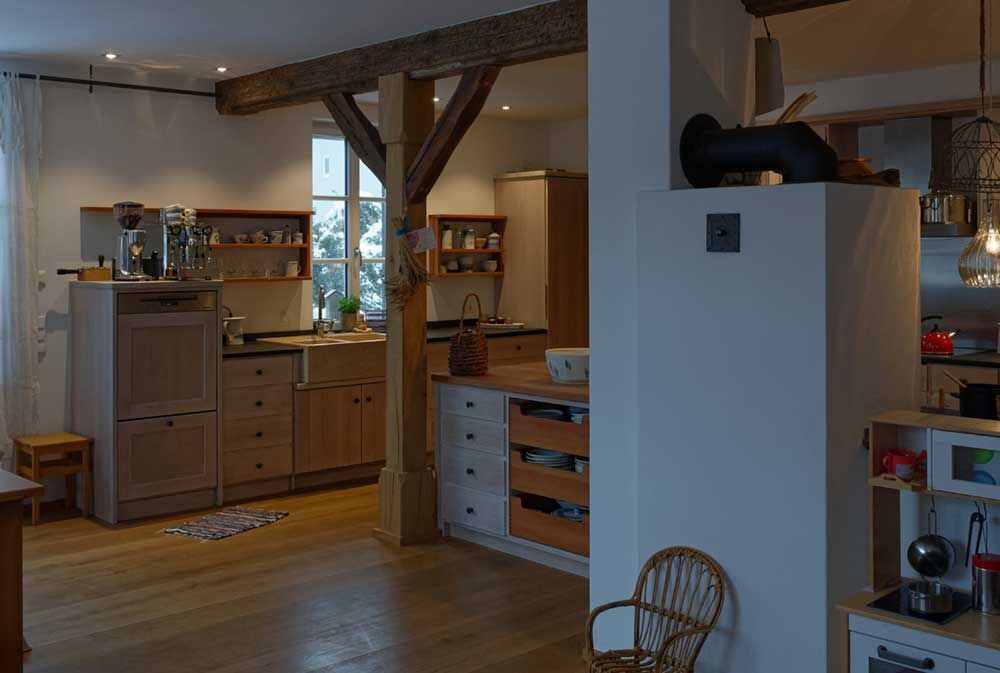 Holzküche mit hellen Schränken, Holzbalken und einer Landhausspüle.