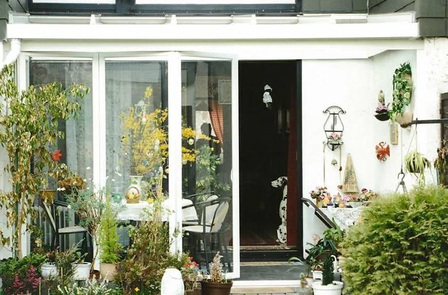 Ein weißes Haus mit einer Glasschiebetür, umgeben von Topfpflanzen