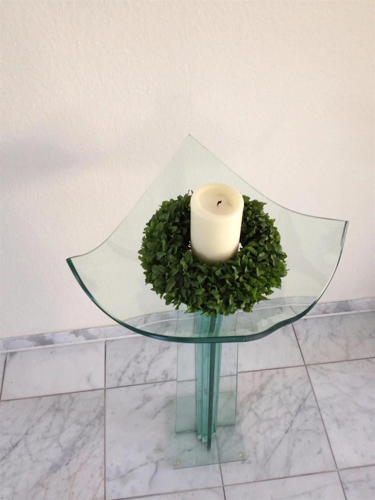 Eine Kerze steht auf einem Glastisch mit einem Kranz darum