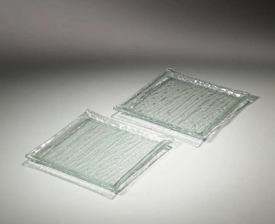 Zwei quadratische Glasplatten liegen übereinander auf einem Tisch.