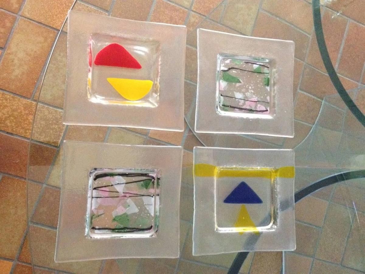 Vier quadratische Teller mit Dreiecken darauf stehen auf einem Glastisch