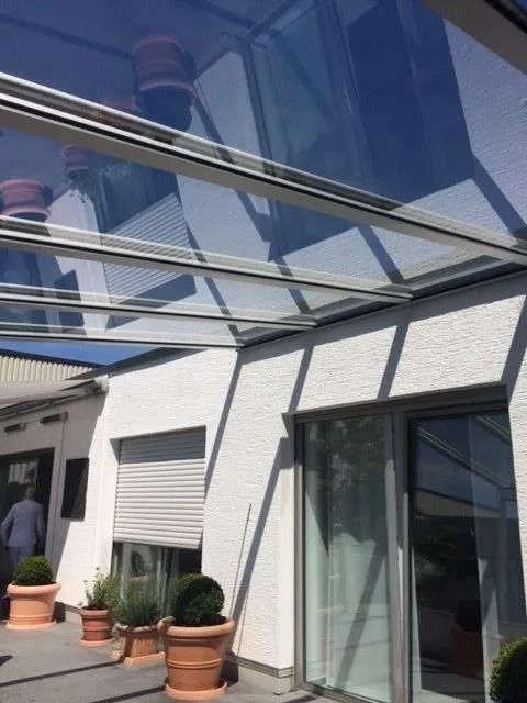 Ein weißes Gebäude mit einem Glasdach und Topfpflanzen davor.