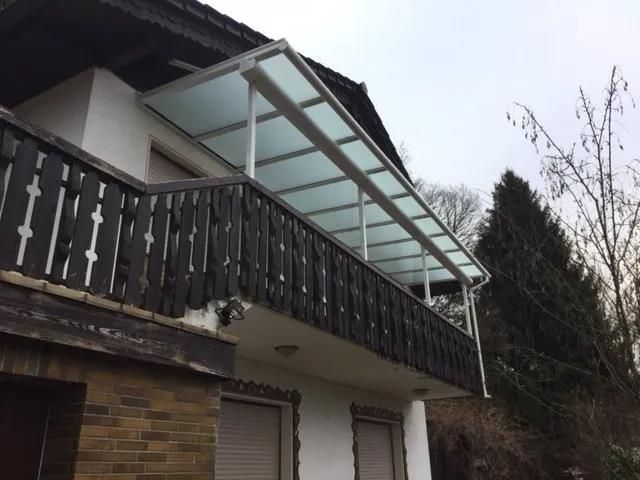 Ein Balkon mit Glasdach und Holzgeländer an der Seite eines Hauses.