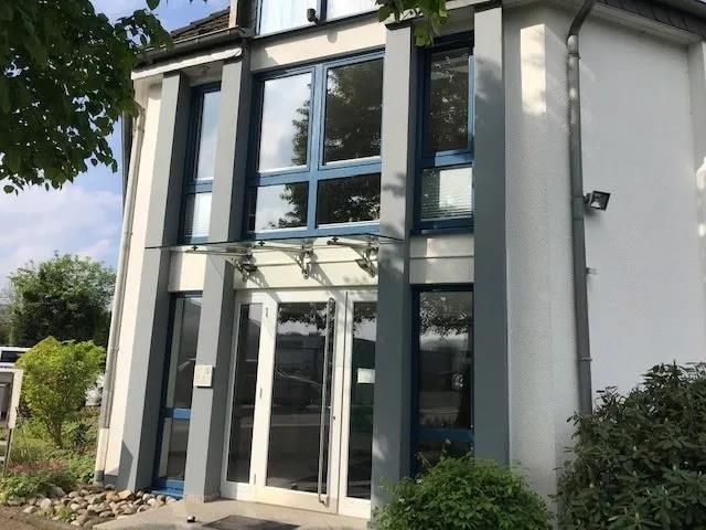 Ein weißes Gebäude mit blauen Fenstern und einem Vordach über dem Eingang.