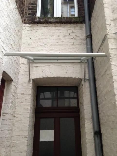 Ein weißes Backsteingebäude mit einer braunen Tür und einem Vordach darüber.