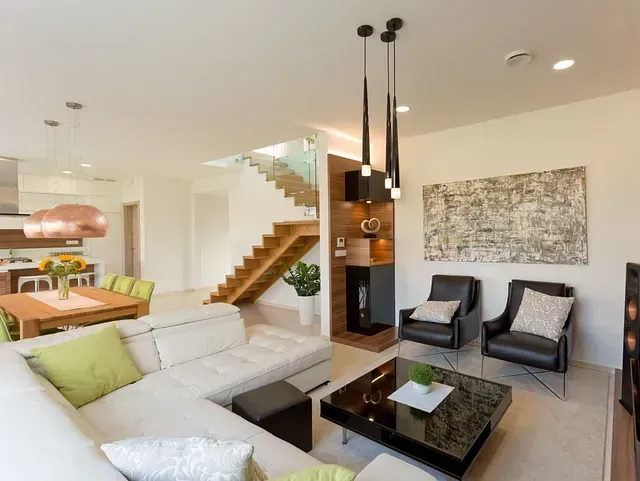 Sala de estar moderna con paredes blancas, sofá seccional, escalera y sillas con detalles oscuros.