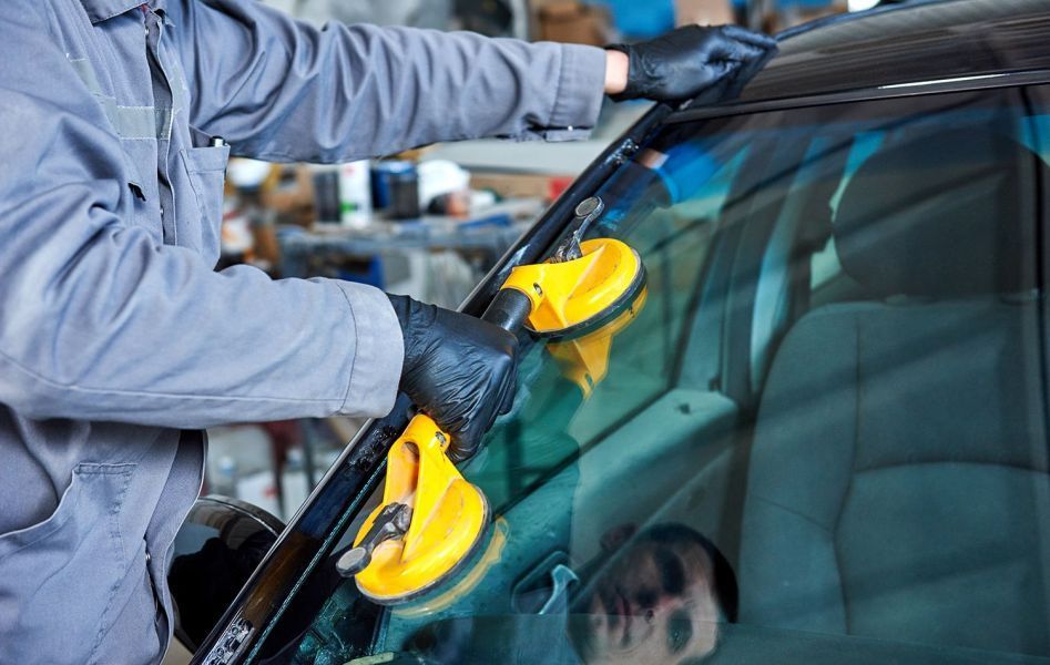 Ein Mechaniker in einer Werkstatt verwendet Saugnäpfe, um eine Windschutzscheibe an einem Auto anzubringen.