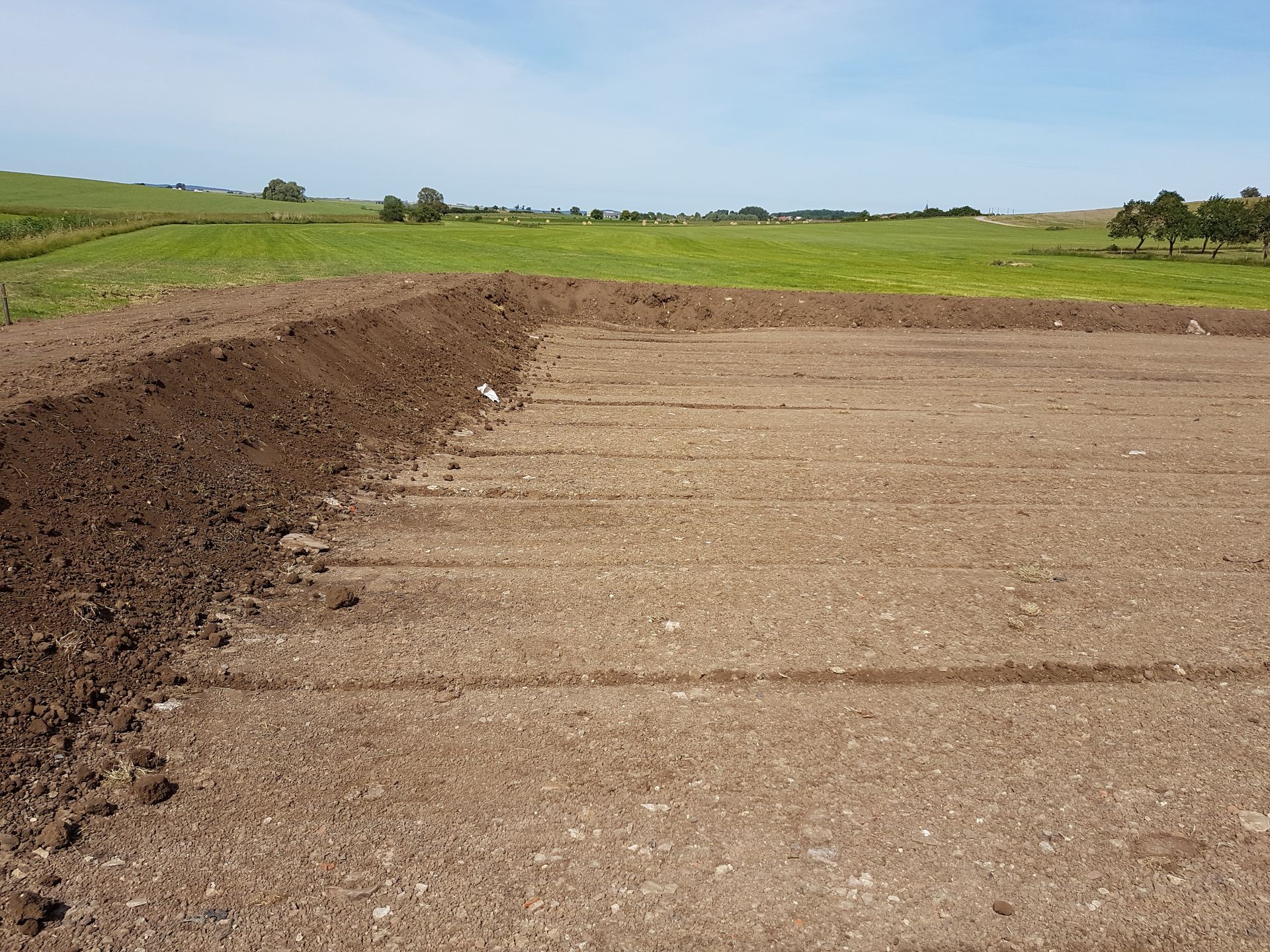 Chemin de gravier serpentant le long d'un talus de terre à travers des champs verdoyants sous un ciel dégagé.