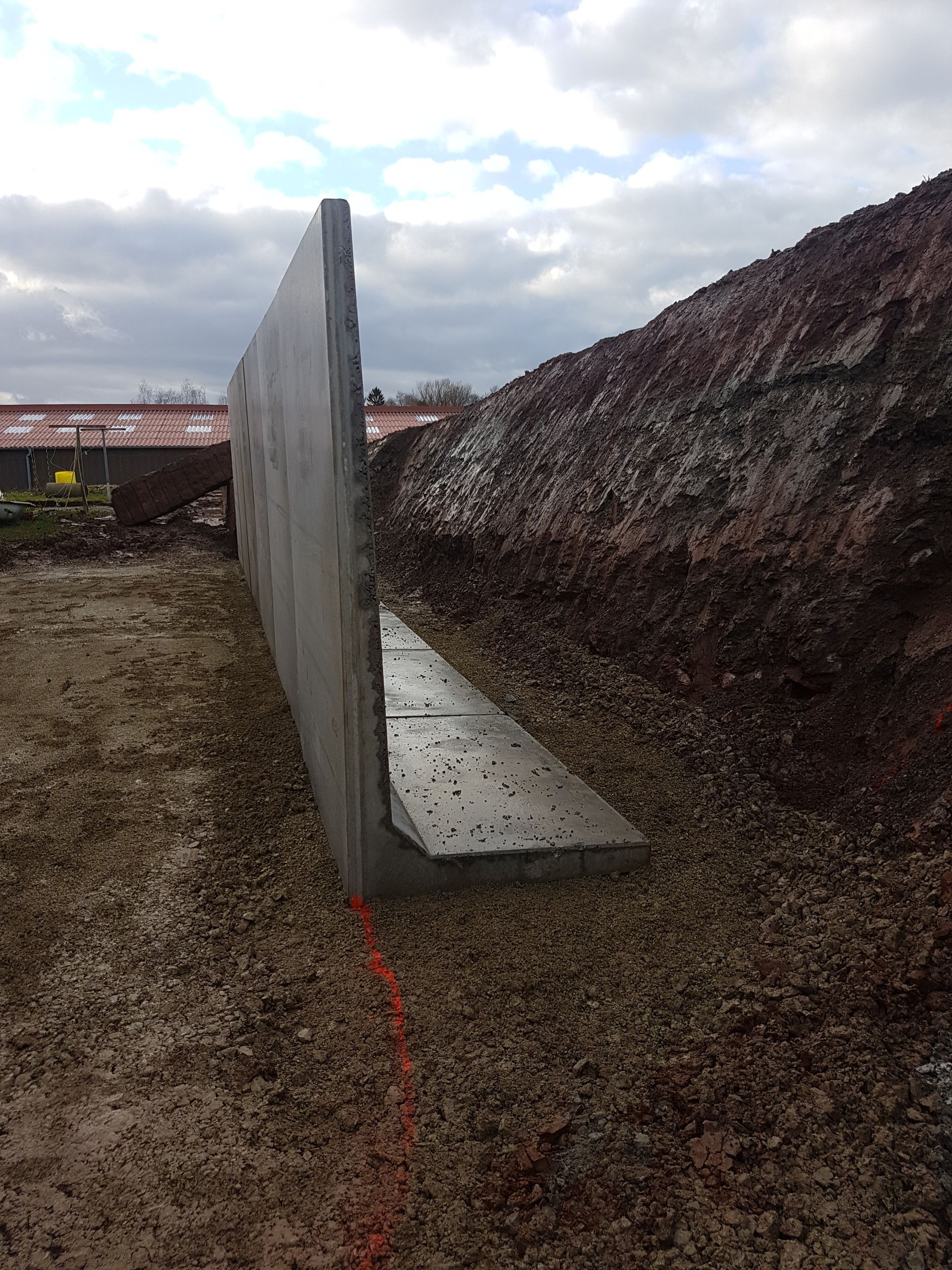 Cloison en béton sur un chantier de construction en terre sous un ciel nuageux.