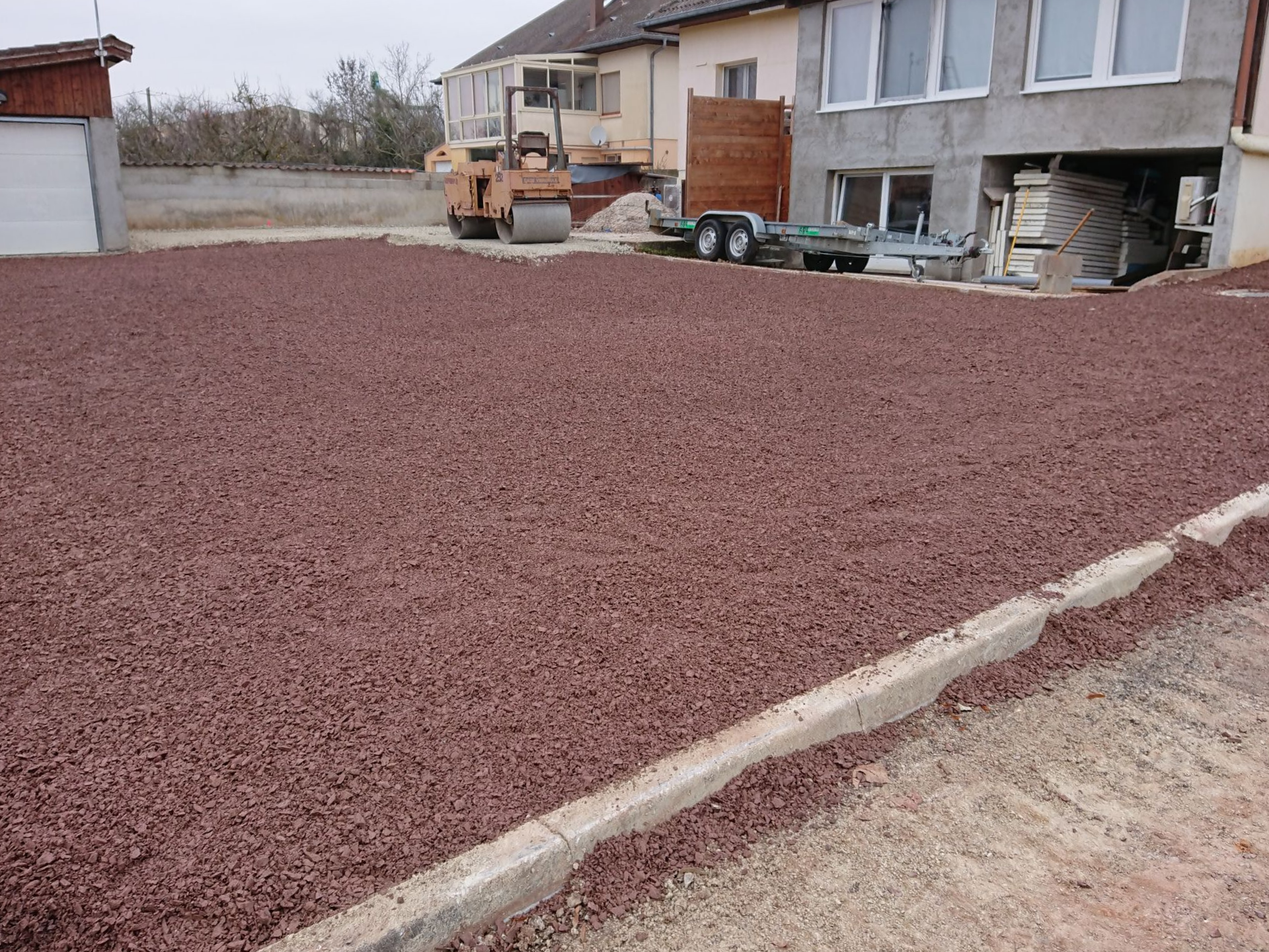 Allée recouverte de gravier à côté d'une maison, avec un petit tracteur et des outils près du mur.
