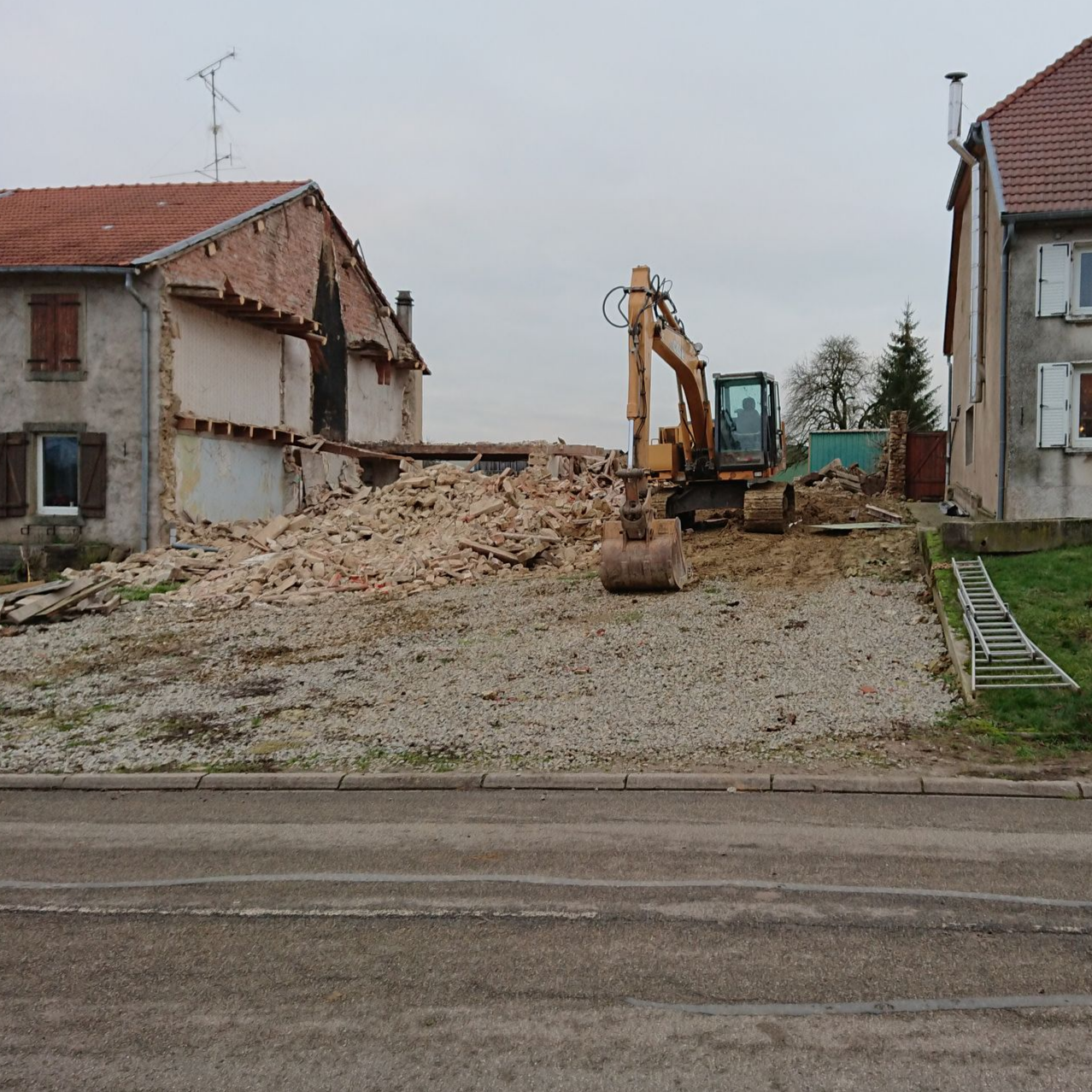 Une pelleteuse au milieu des décombres entre deux maisons endommagées sur un chantier de démolition.