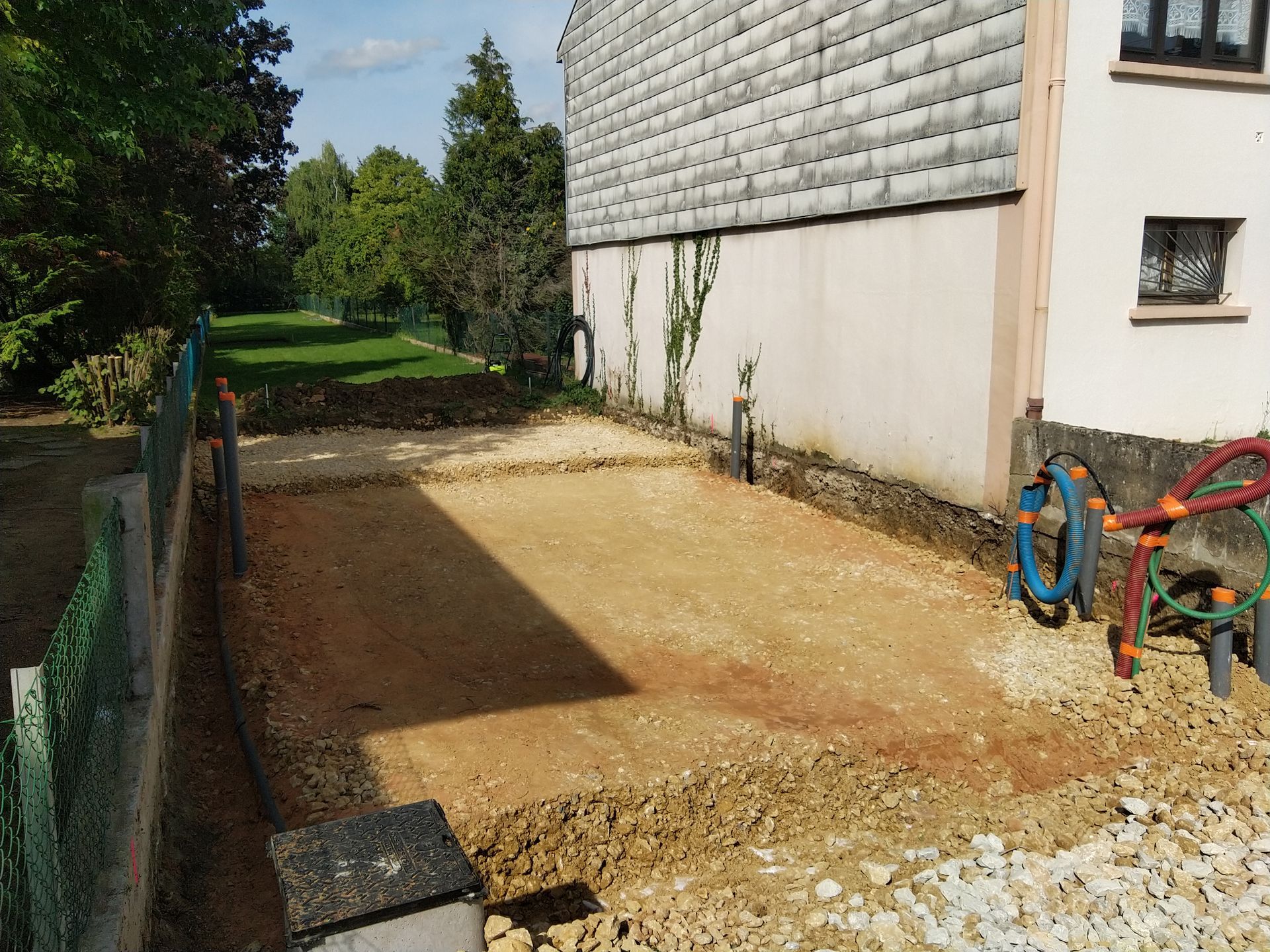 Allée de terre à côté d'un bâtiment blanc, avec la verdure en arrière-plan.