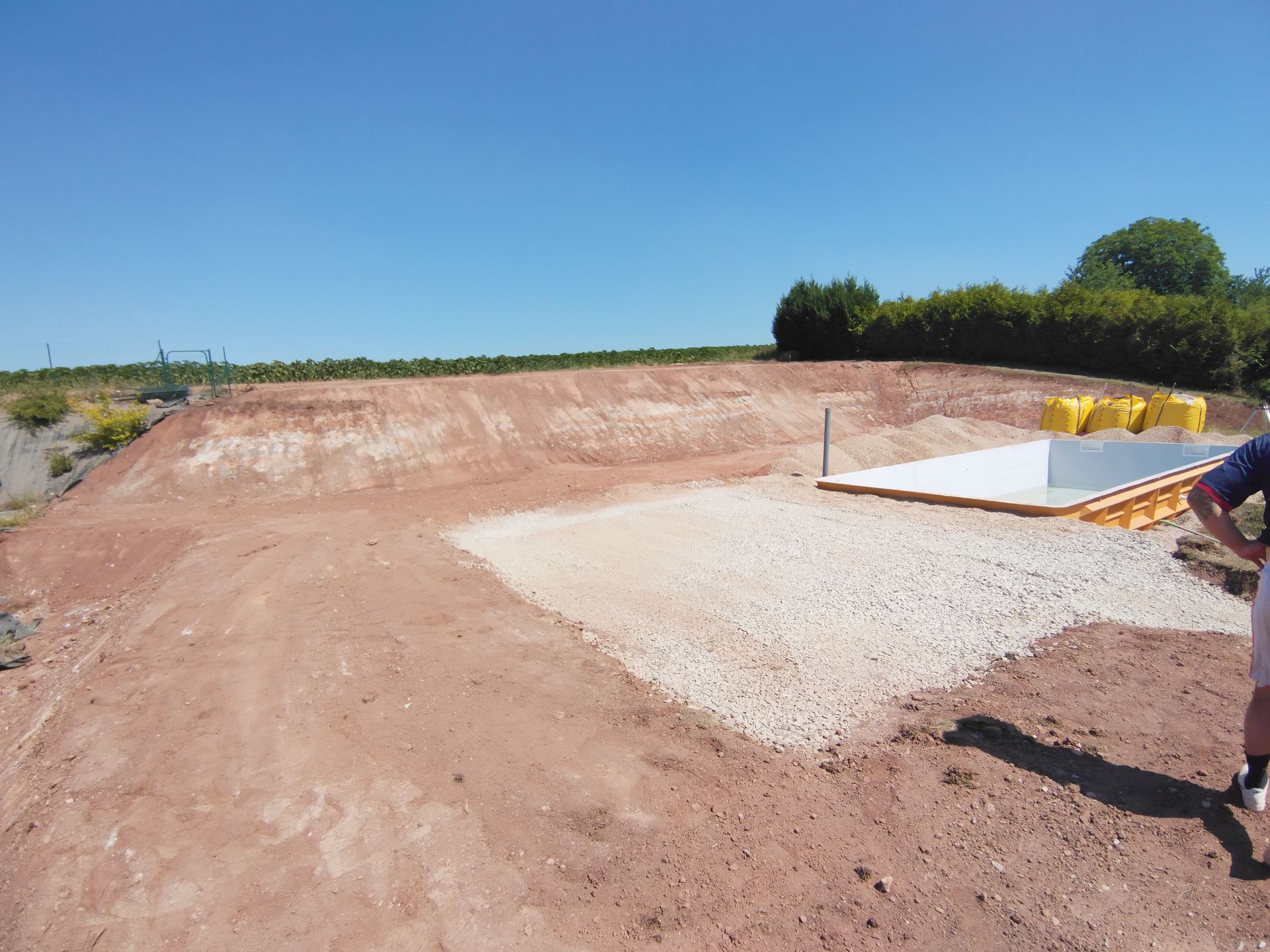 Chantier de construction avec terrain nivelé, dalle de gravier et sous un ciel bleu dégagé.