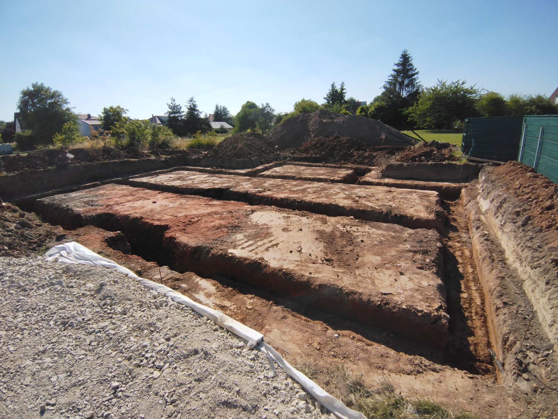 Tranchées d'excavation et tas de terre sur un chantier de construction sous un ciel bleu dégagé.