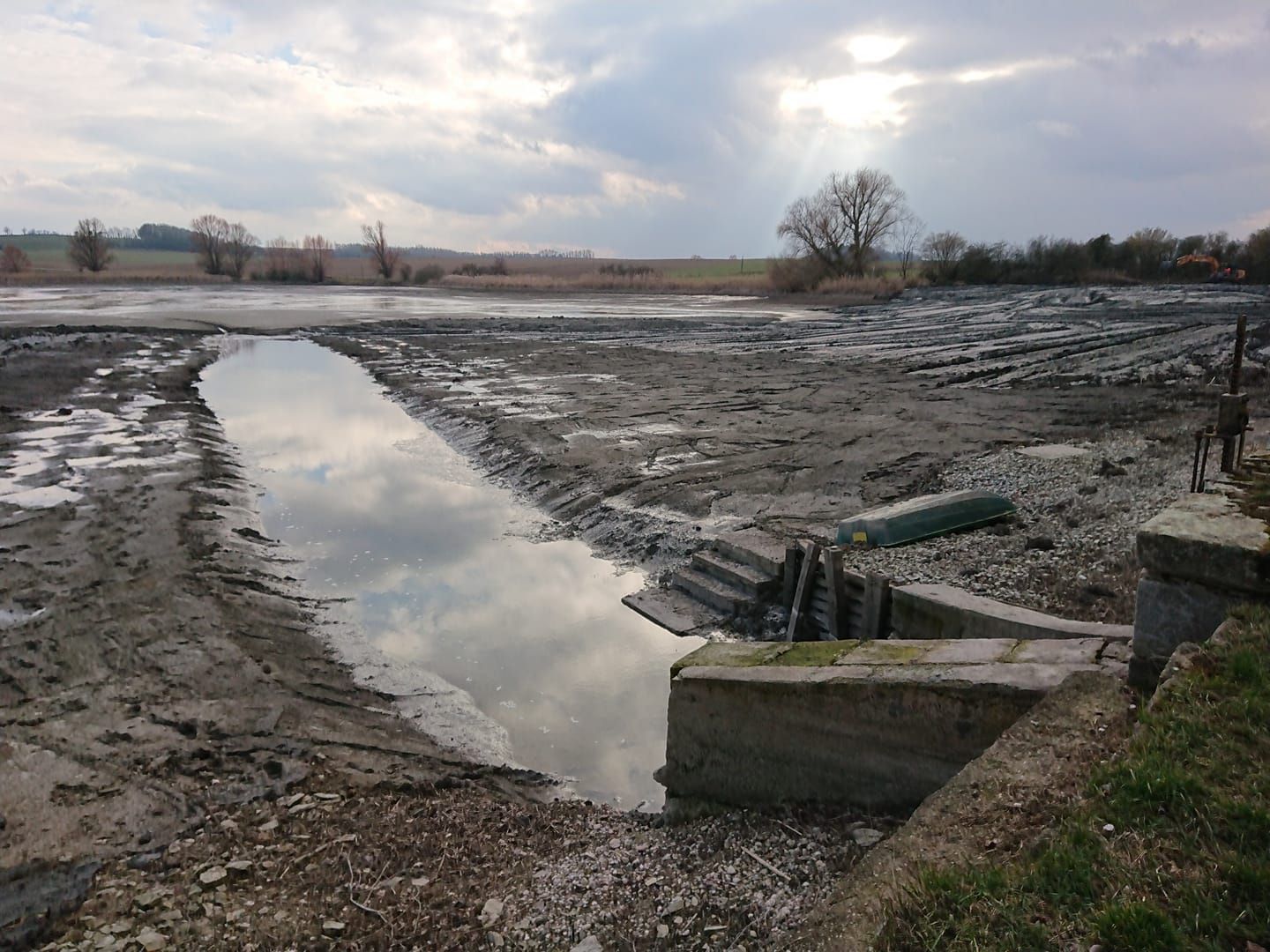 Champ boueux inondé avec un étroit chenal d'eau réfléchissante sous un ciel nuageux.