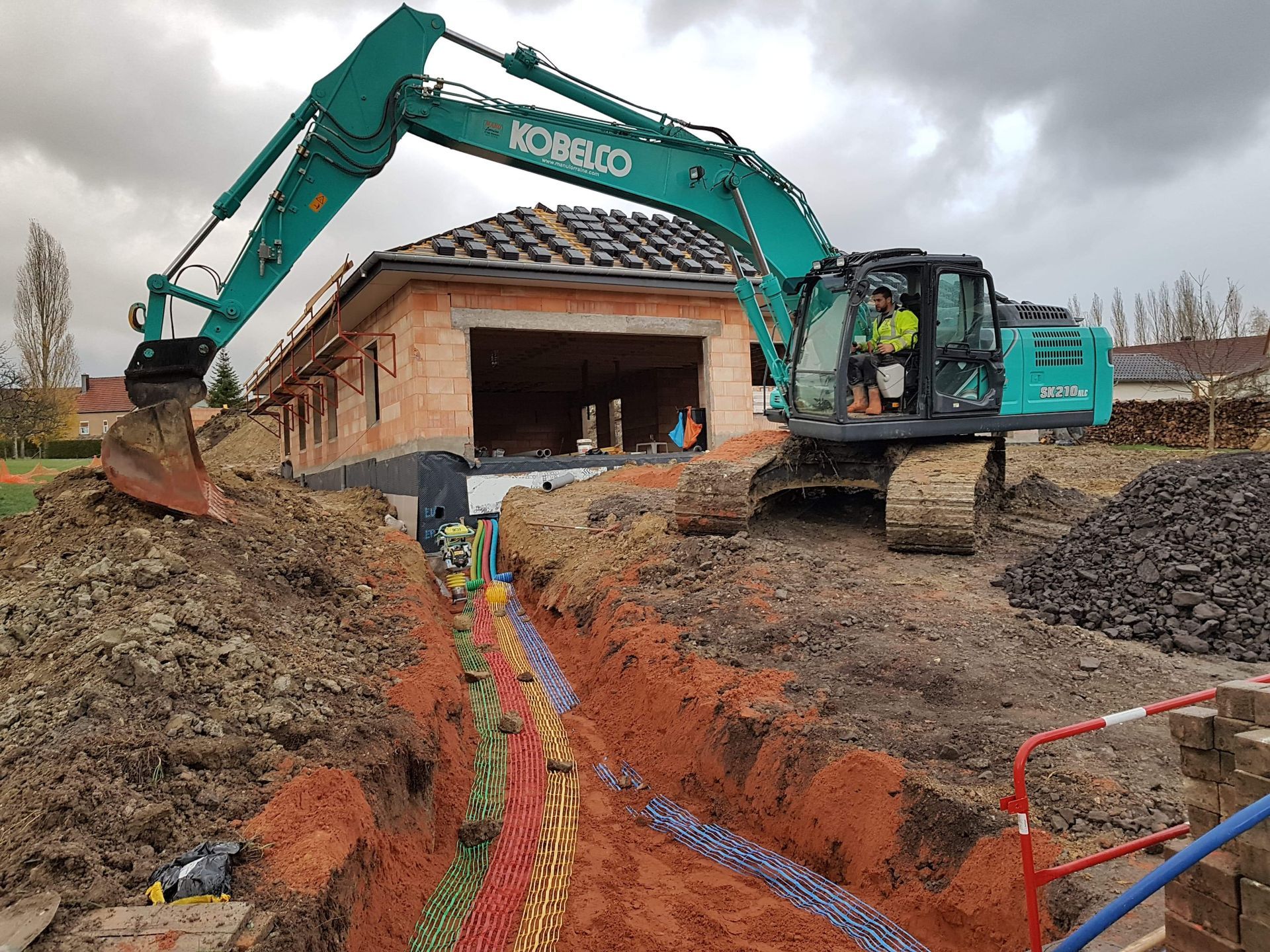 Une pelleteuse creuse une tranchée à côté d'un bâtiment en briques sur un chantier de construction.