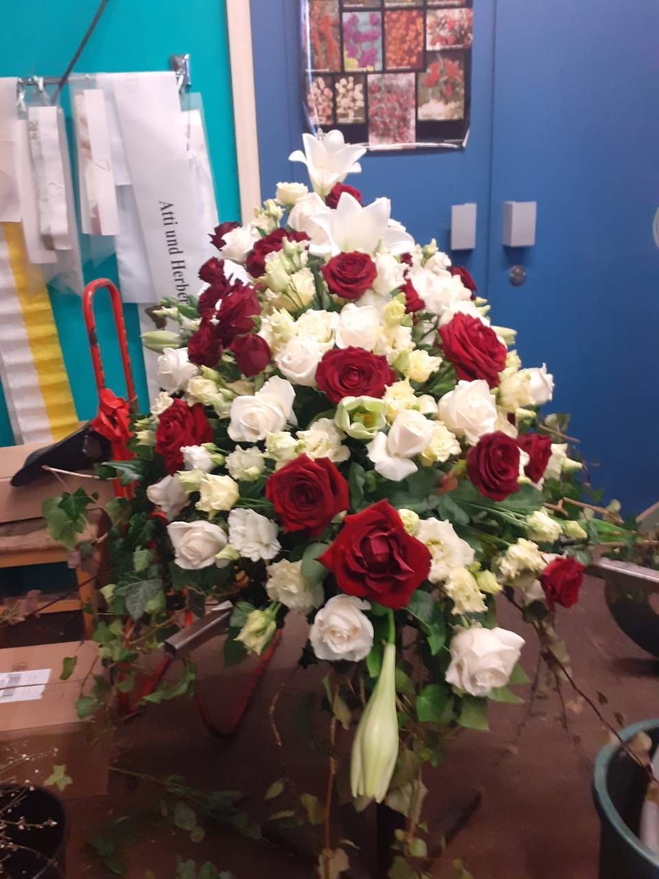 Blumenarrangement mit weißen Lilien, roten und weißen Rosen und Grünzeug.