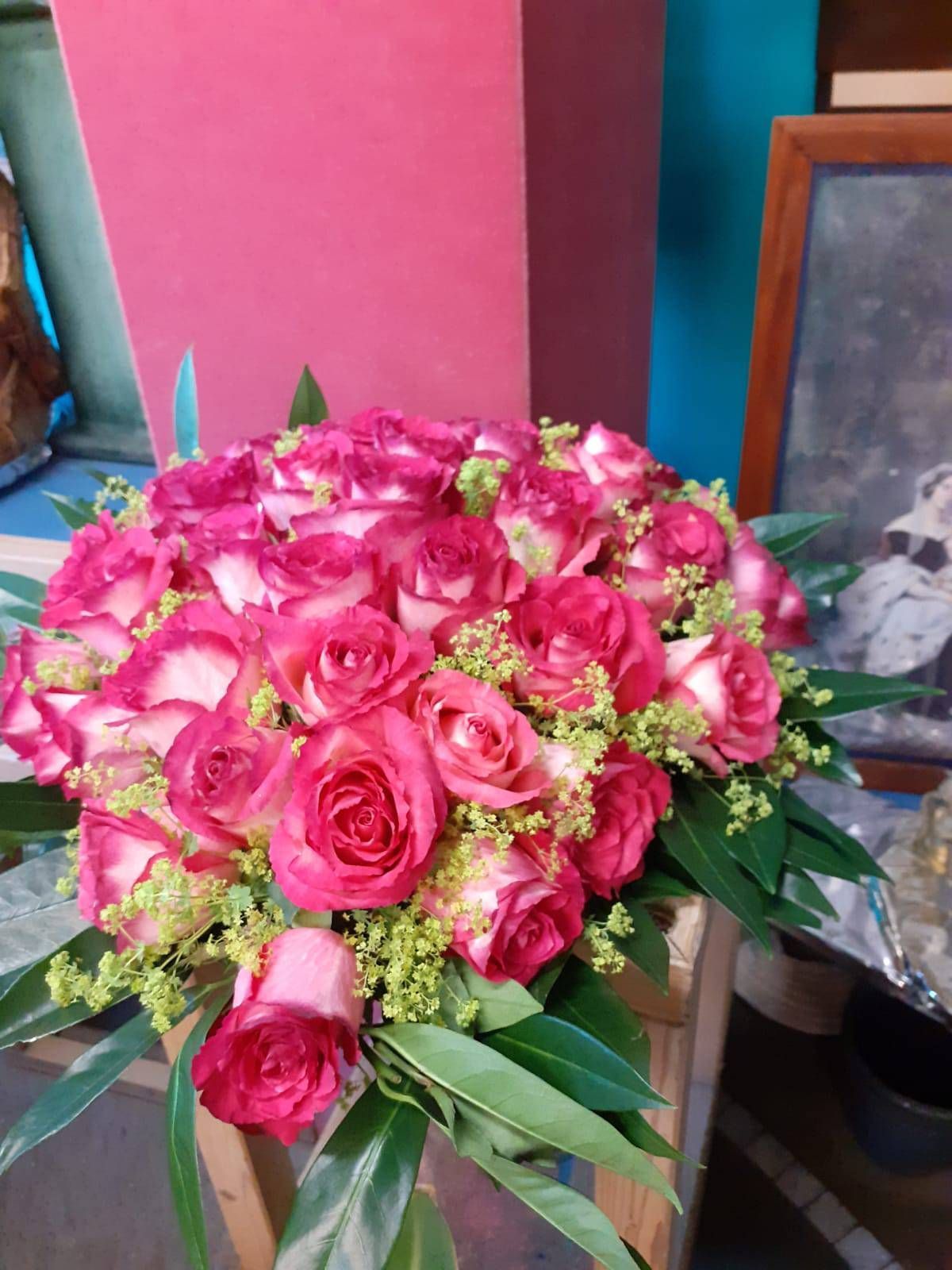 Nahaufnahme eines Straußes aus rosa und weißen Rosen mit grünem Füllmaterial, der auf einer Holzoberfläche steht.