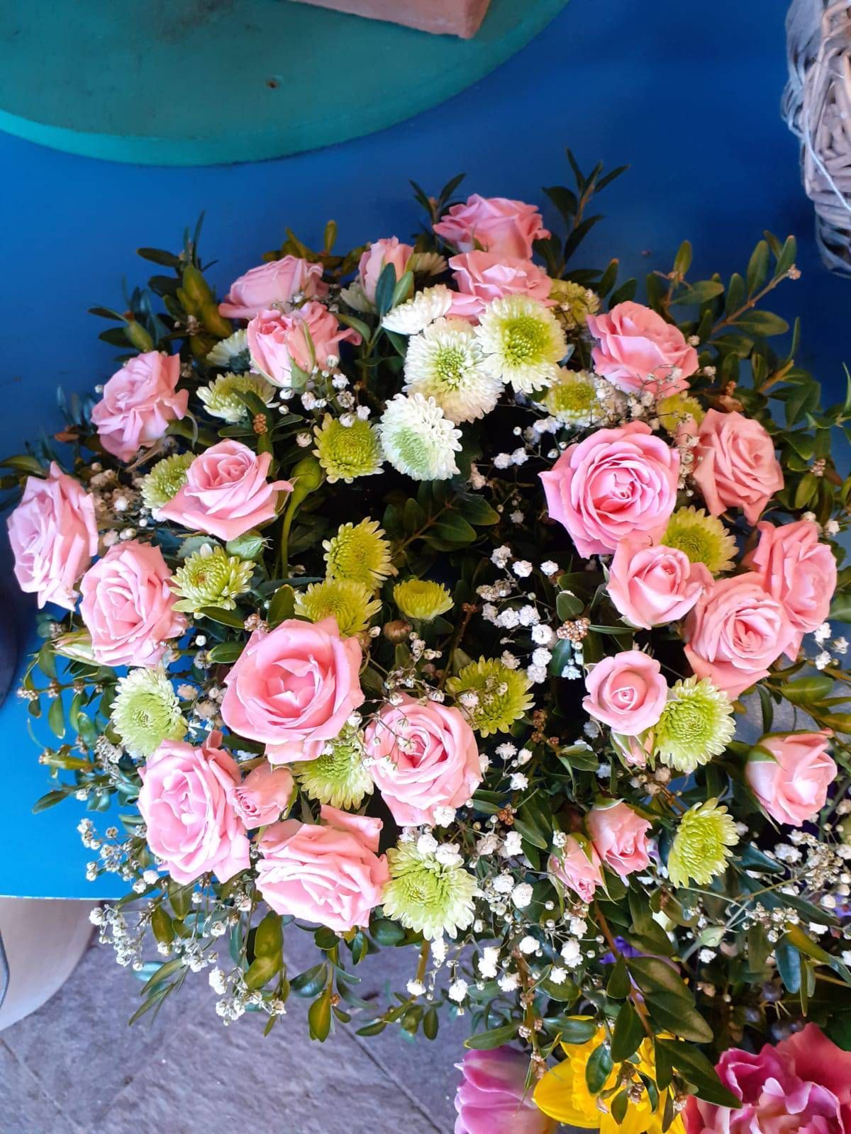 Rosa Rosen und grüne Chrysanthemen in einem Blumenarrangement, mit weißem Schleierkraut, vor blauem Hintergrund.