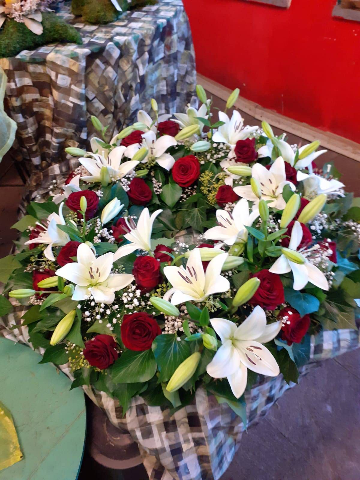 Ein Kranz aus weißen Lilien und roten Rosen auf einem karierten Tisch.