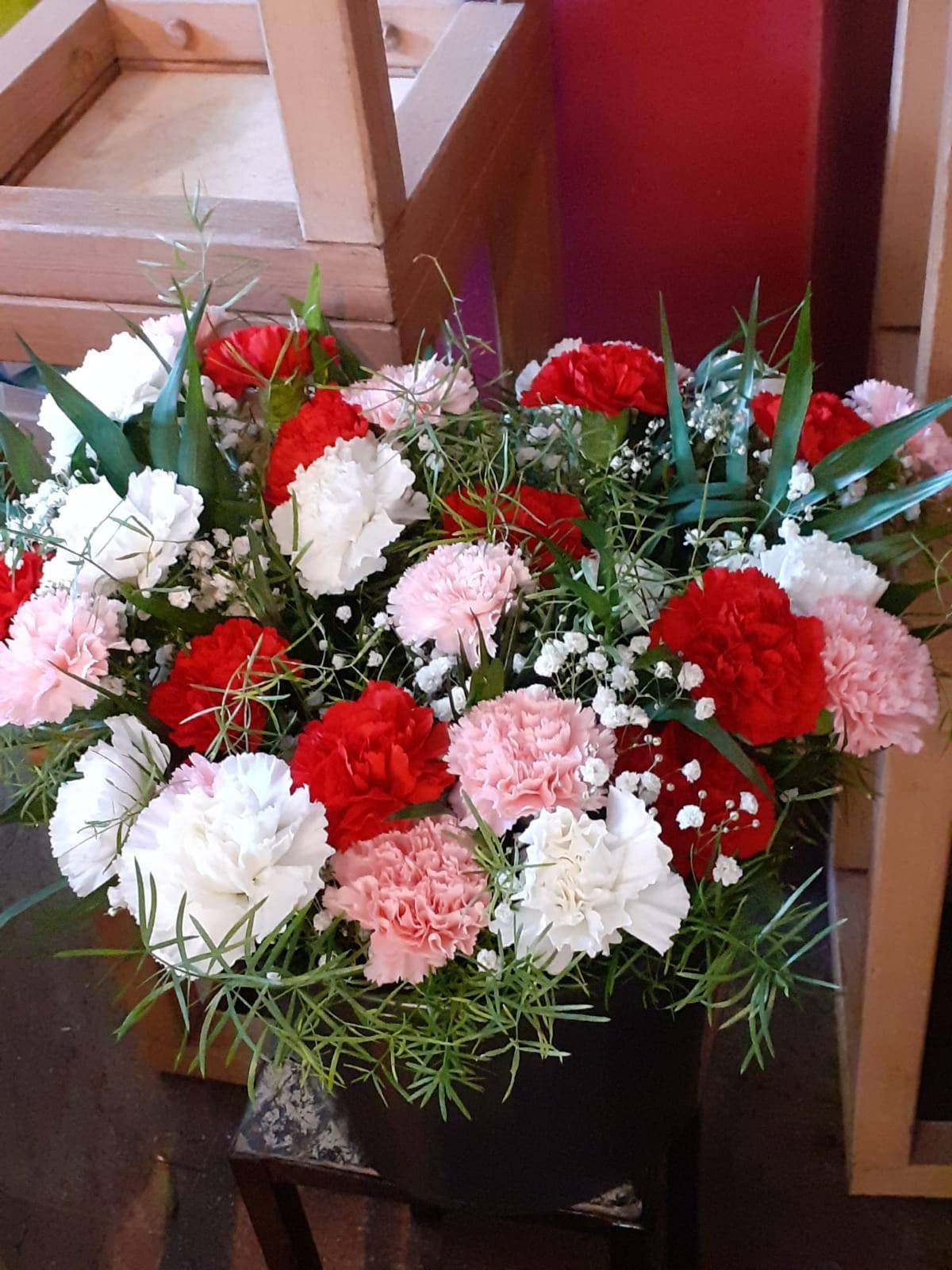 Bunte Nelken, Schleierkraut und Grünzeug in einer schwarzen Vase, die auf einer Holzoberfläche steht.