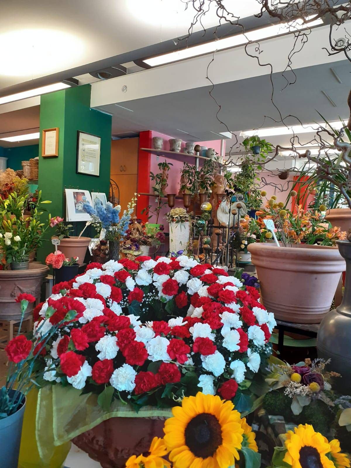 Innenansicht eines Blumengeschäfts mit einem ausgestellten rot-weißen Nelkenkranz.