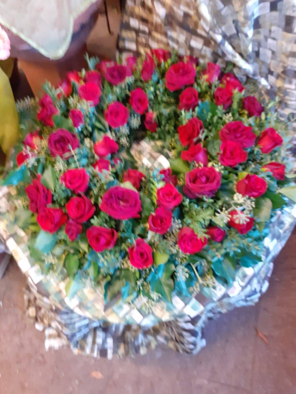 Ein Kranz aus roten Rosen und grünem Laub, umwickelt mit gemustertem Papier.