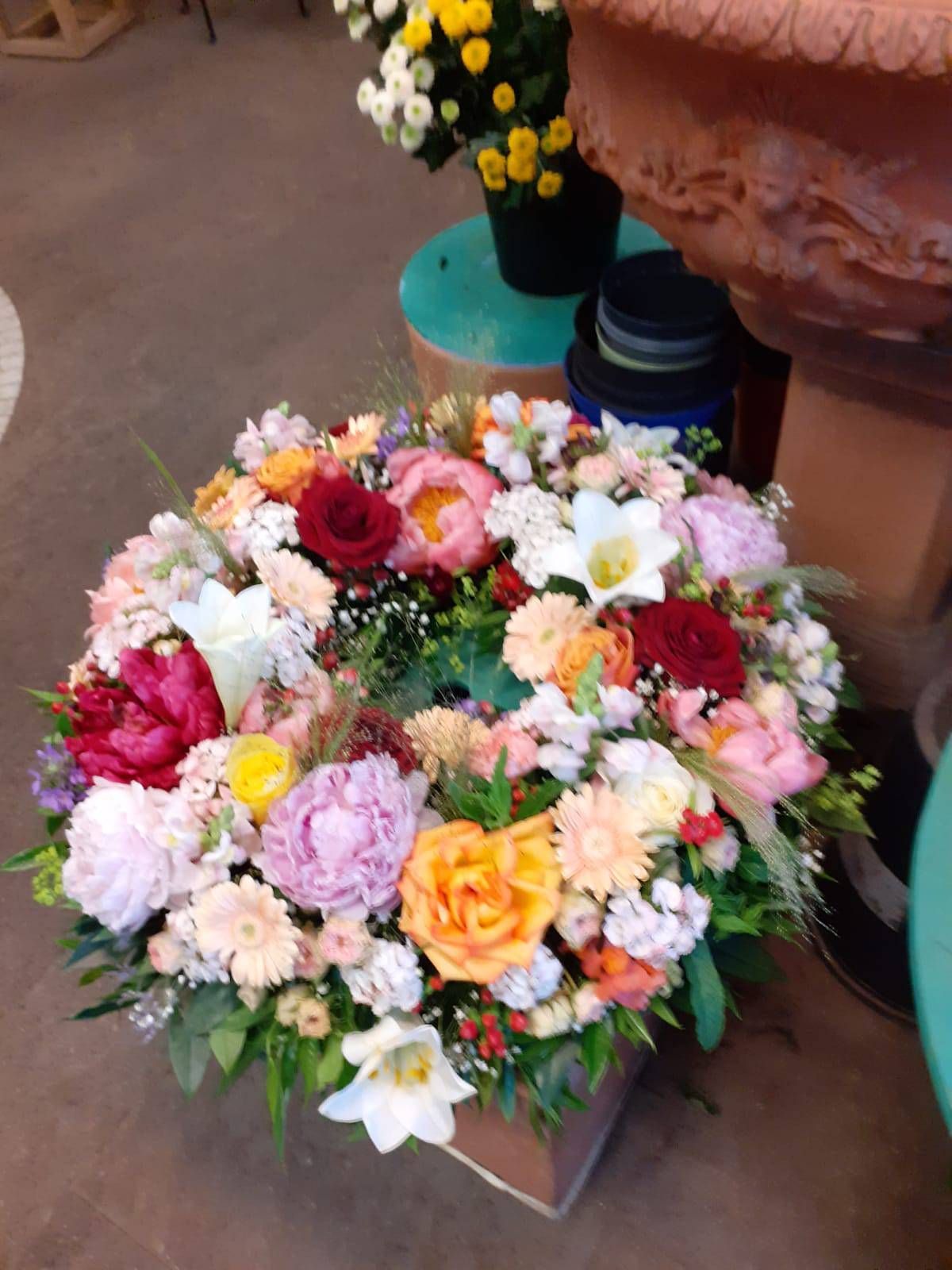 Ein farbenfrohes Blumenarrangement in einer Holzbox mit bunten Pfingstrosen, Rosen und Grünpflanzen.