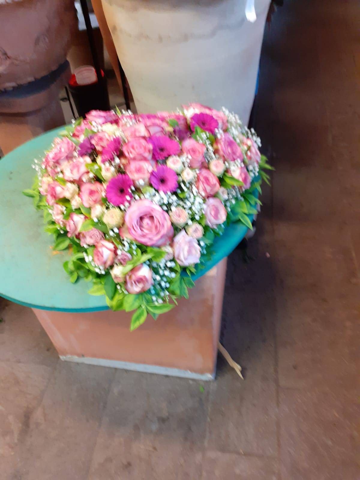 Herzförmiges Blumenarrangement aus rosa Rosen und Grünzeug auf türkisfarbenem Untergrund.