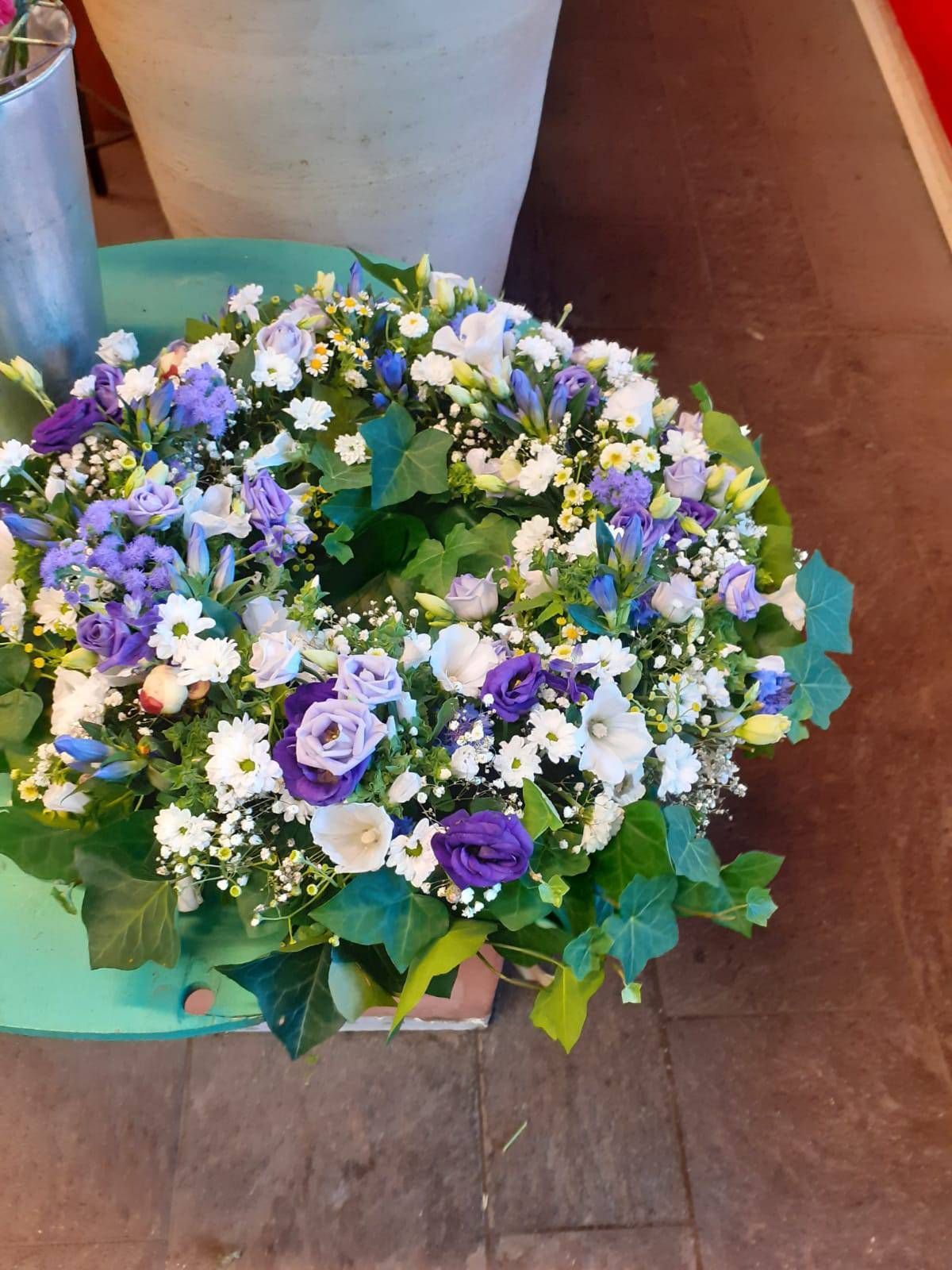 Kranz aus weißen und violetten Blüten mit Grünzeug auf grünem Untergrund.