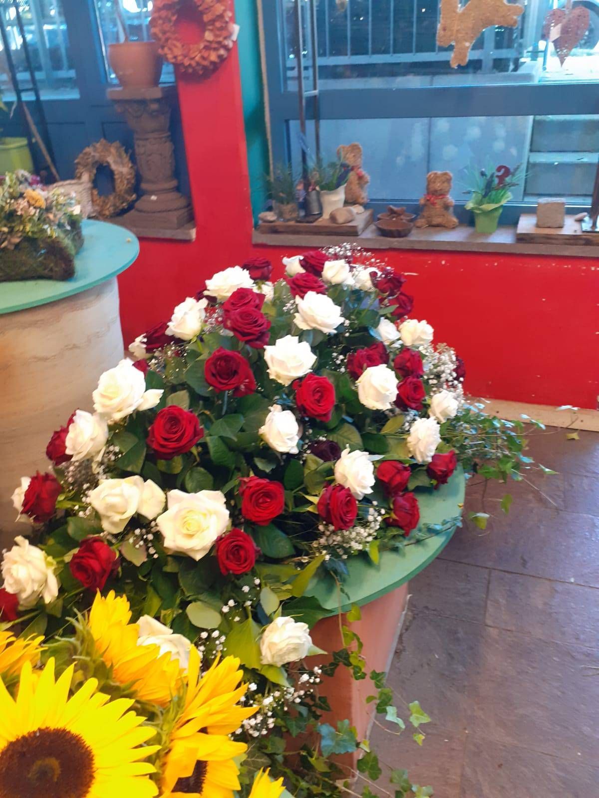 Ein Arrangement aus roten und weißen Rosen und Grünzeug in einem Blumenladen. Sonnenblumen im Vordergrund.