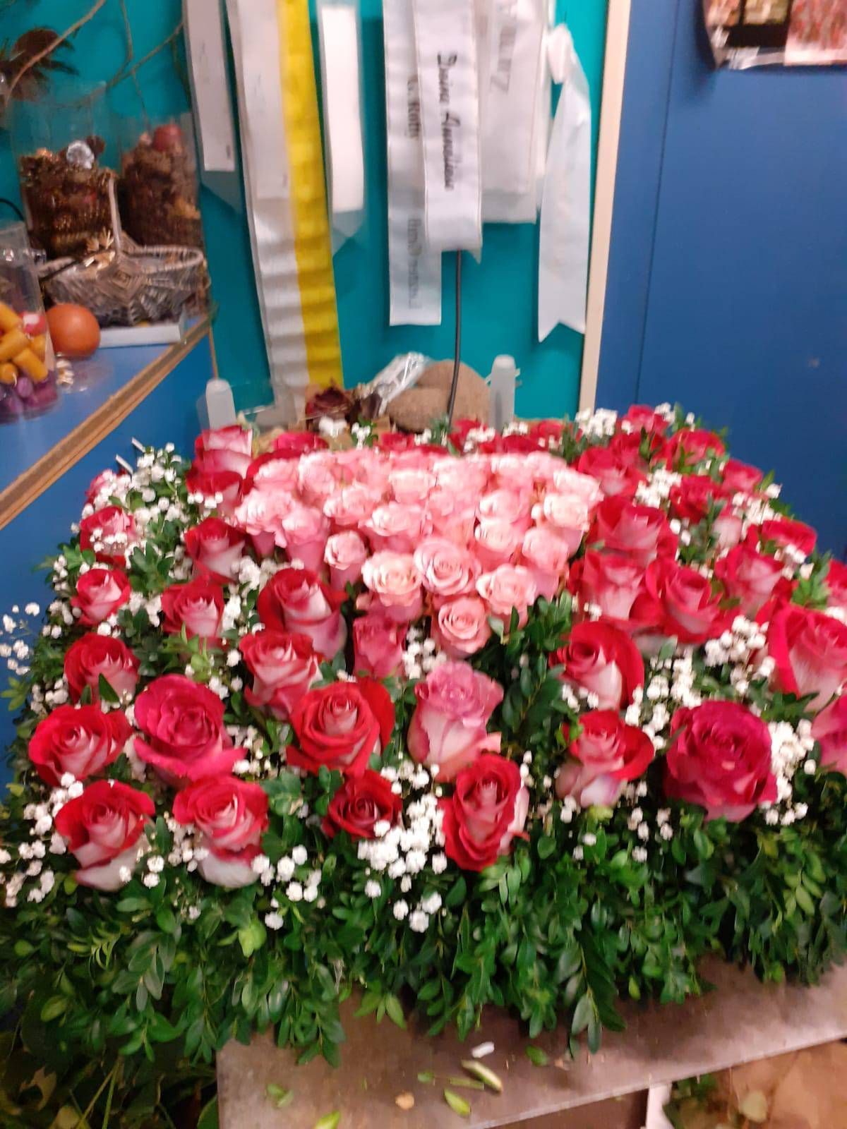 Herzförmiges Blumenarrangement mit rosa und roten Rosen, umgeben von Grünzeug und Schleierkraut.