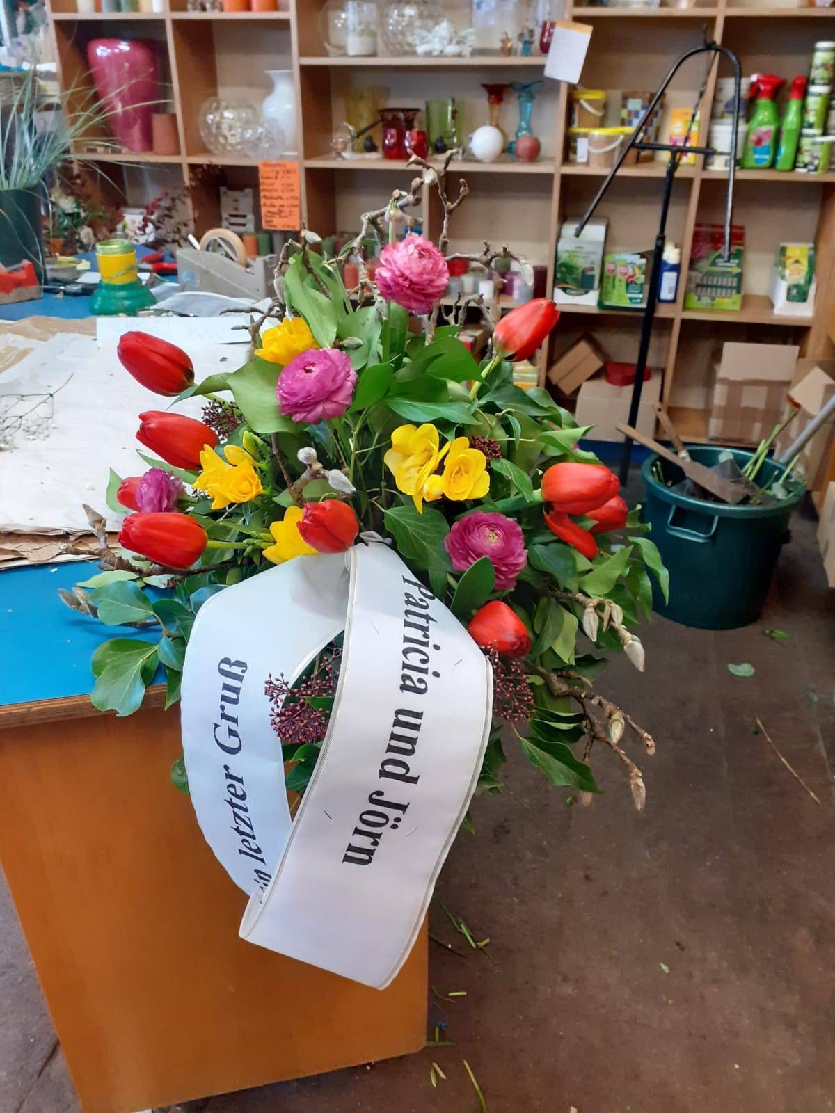 Farbenfrohes Blumenarrangement mit einem weißen Band mit der Aufschrift „Patricia und Jörn“ in einem Blumenladen.