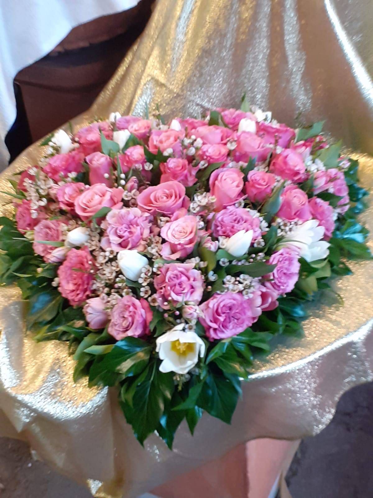 Herzförmiges Blumenarrangement mit rosa Rosen, weißen Tulpen und Grünzeug auf goldenem Stoff.