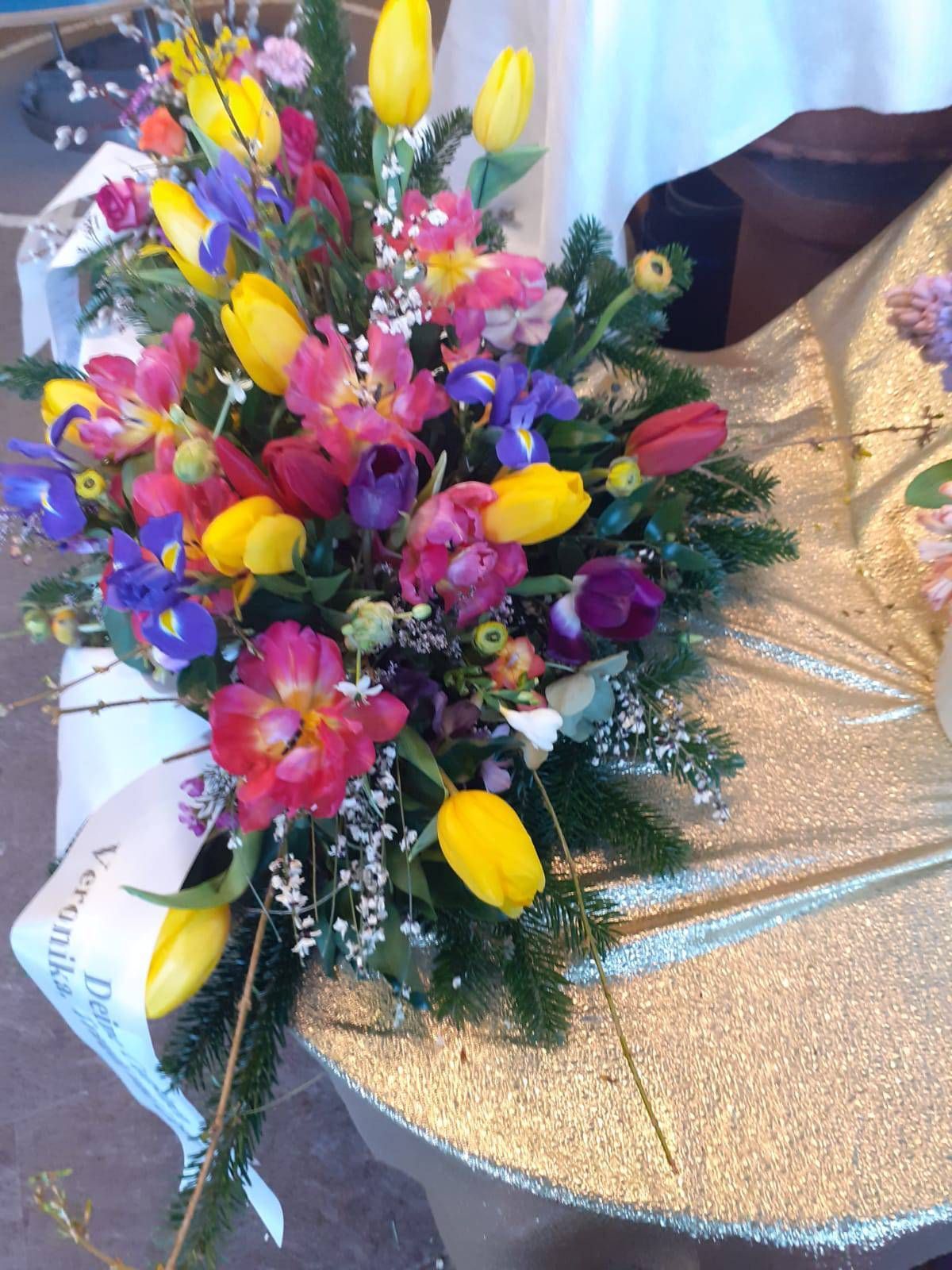 Strauß aus gelben Tulpen, rosa und violetten Blumen sowie blauen Schwertlilien; inklusive Grünzeug und weißem Band.