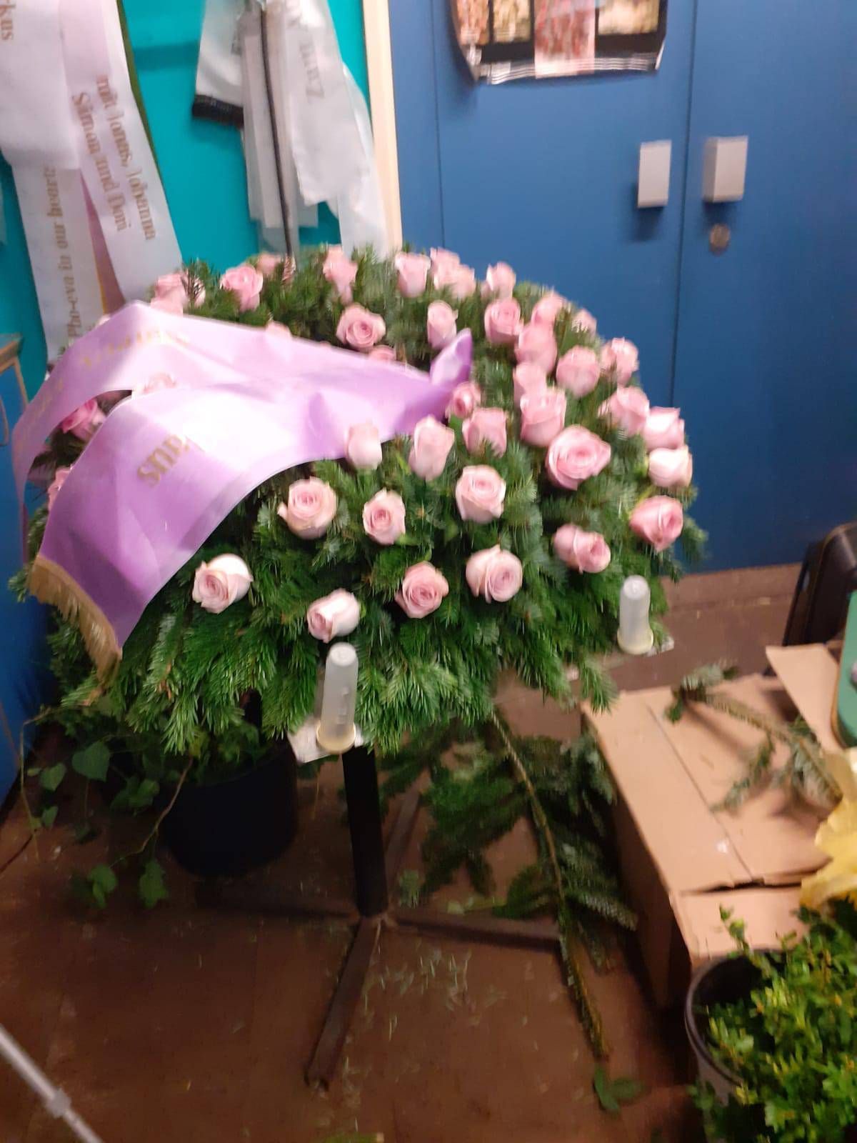 Ein Blumenkranz aus rosa Rosen und Grünzeug mit einem violetten Band.