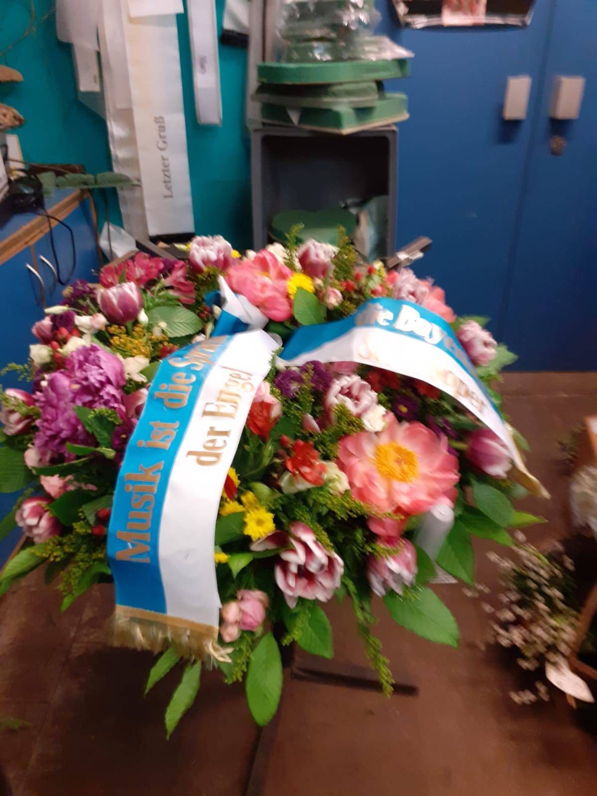 Ein bunter Blumenkranz mit einem blau-weißen Band, auf dem 