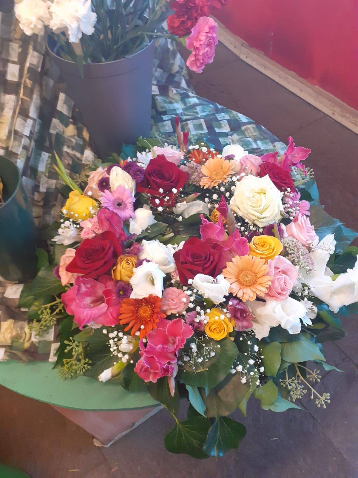 Farbenfrohes Blumenarrangement mit roten, rosa, gelben und orangen Blüten, grünem Laub und weißem Schleierkraut.