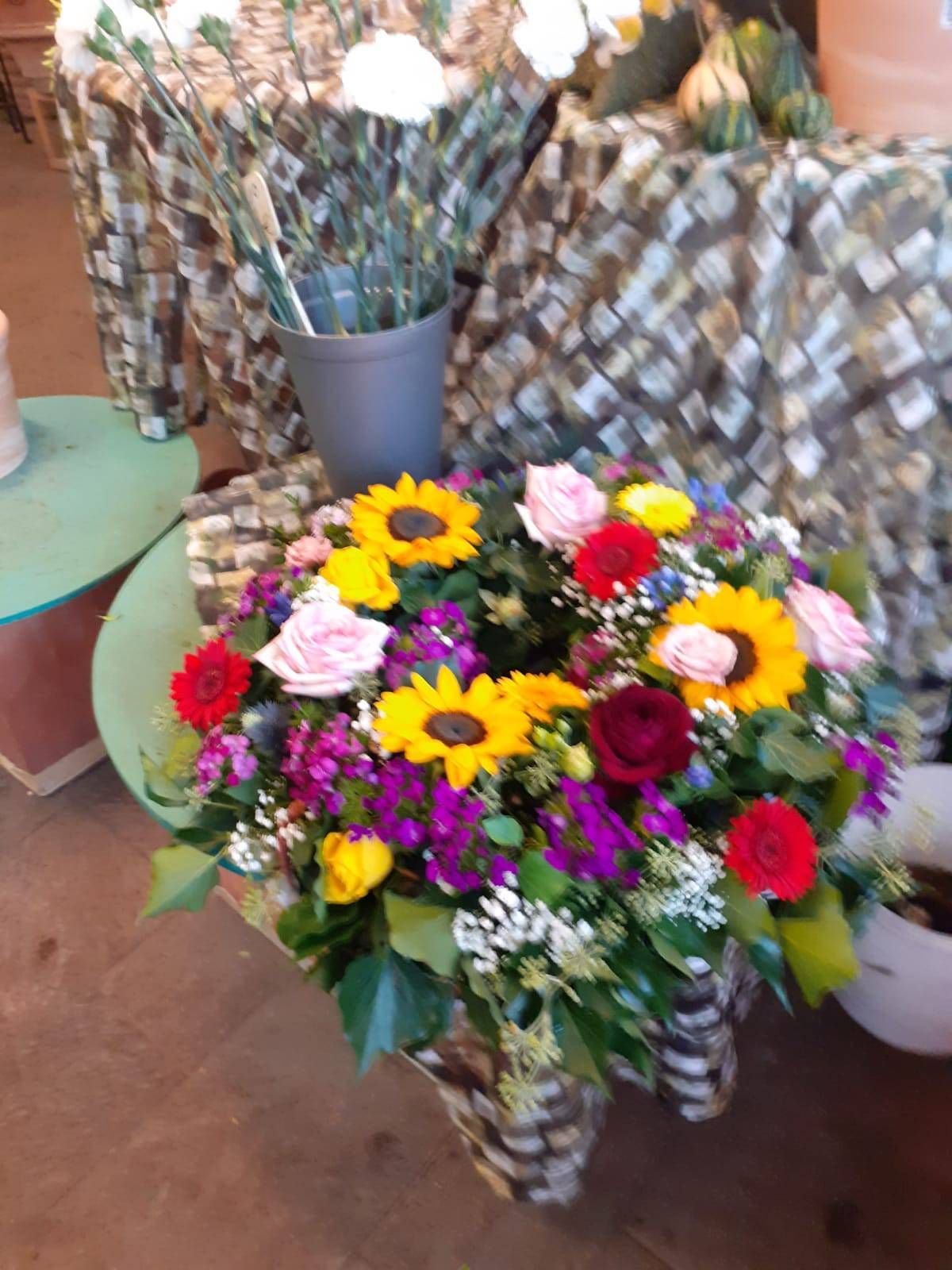 Farbenfrohes Blumenarrangement mit Sonnenblumen, Rosen und anderen Blumen in einem geflochtenen Korb.