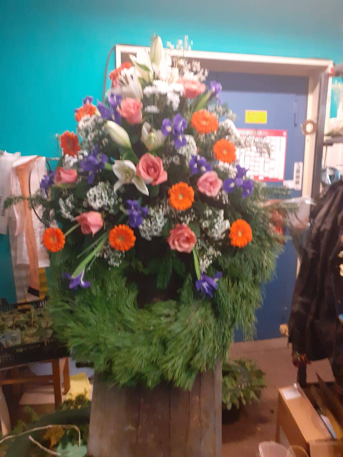 Blumenarrangement: Grüner Kranzrohling mit orangefarbenen, rosafarbenen, violetten und weißen Blüten, für den Innenbereich.