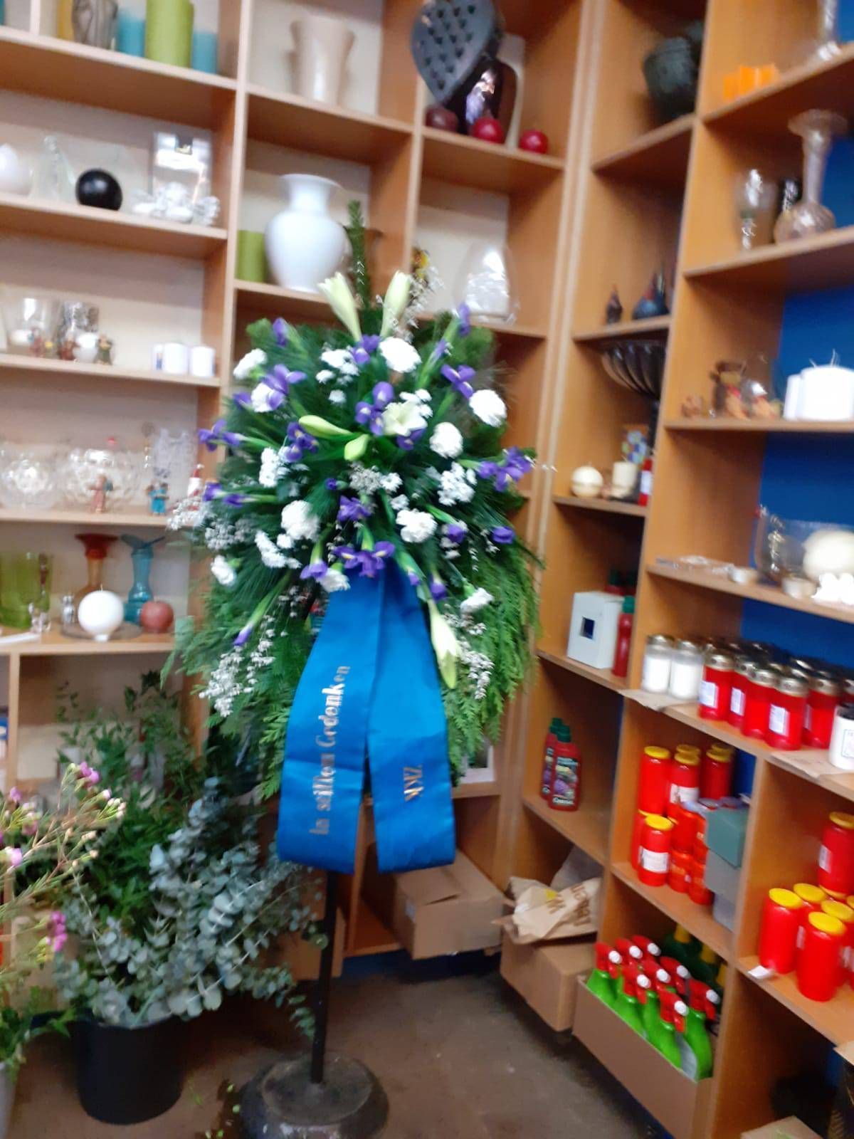 Blumenkranz mit blauem Band in einem Laden mit Regalen voller Waren.
