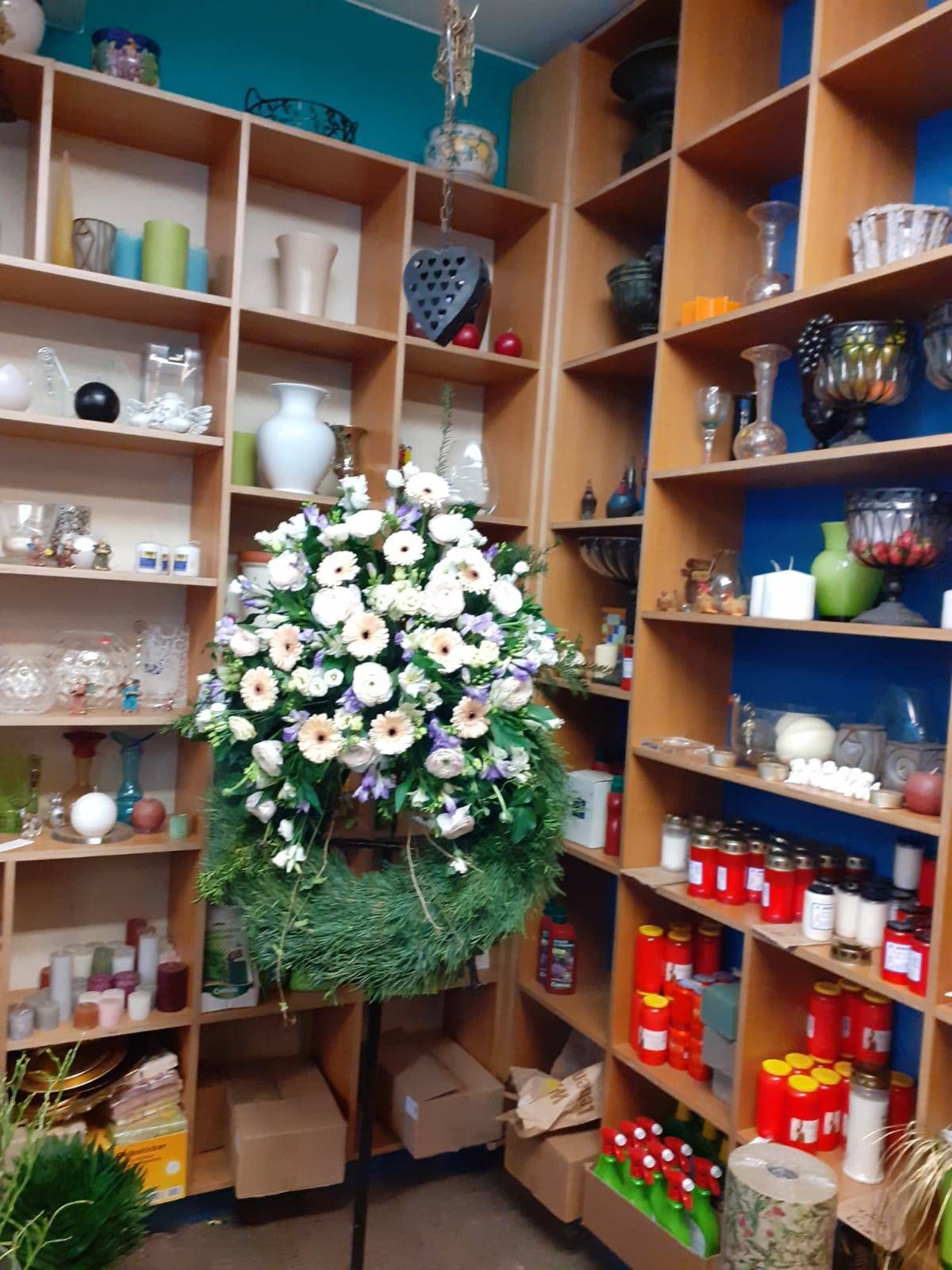 Das Interieur eines Blumenladens mit einem großen Kranz aus weißen Blumen und Regalen voller Kerzen und Vasen.