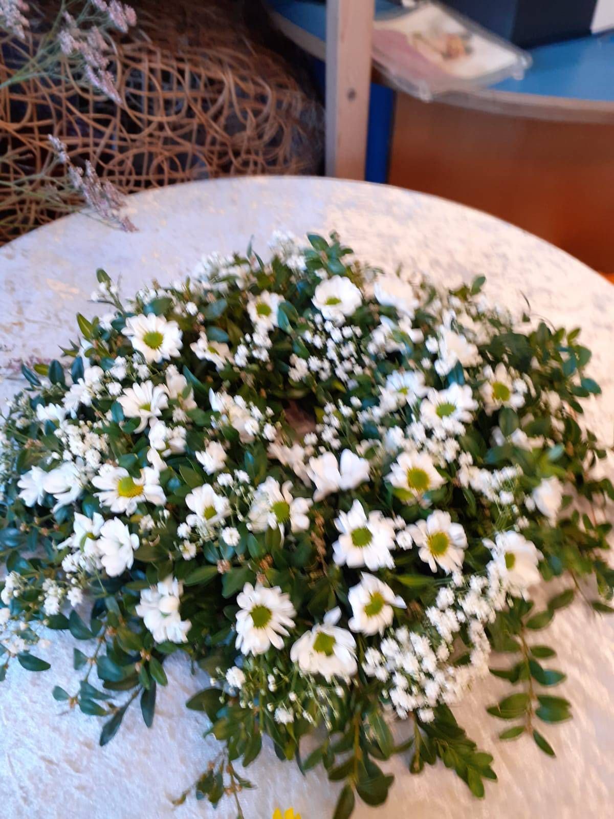 Ein Kranz aus weißen Gänseblümchen und Grünzeug auf einer weißen Tischdecke.