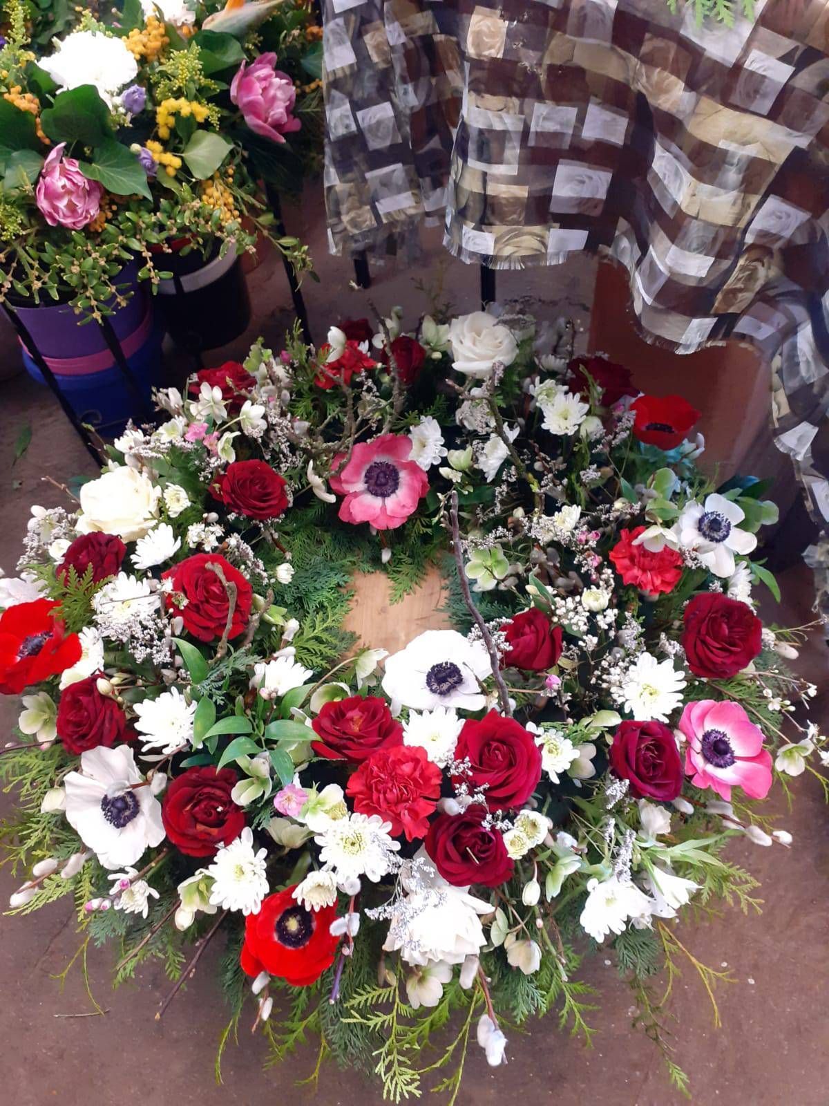Blumenkranz mit roten Rosen, weißen Blüten und Grünzeug.