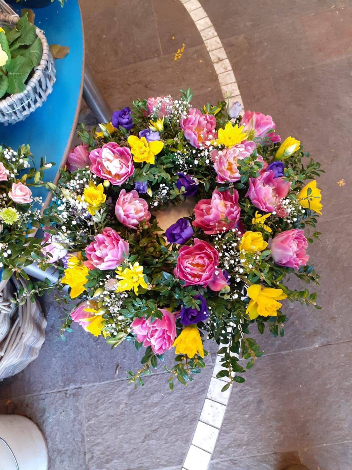 Blumenkranz mit rosa, gelben und violetten Blüten und Grünzeug auf blauem Grund.