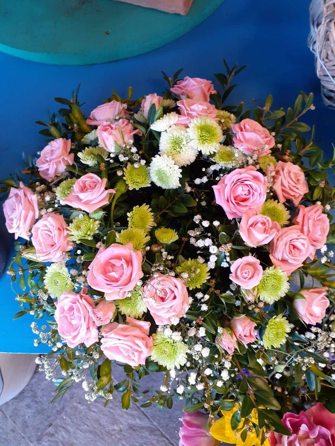 Blumenarrangement mit weißem Band: grüne, rosa und weiße Blumen in einem Korb. Das Band ist beschriftet.