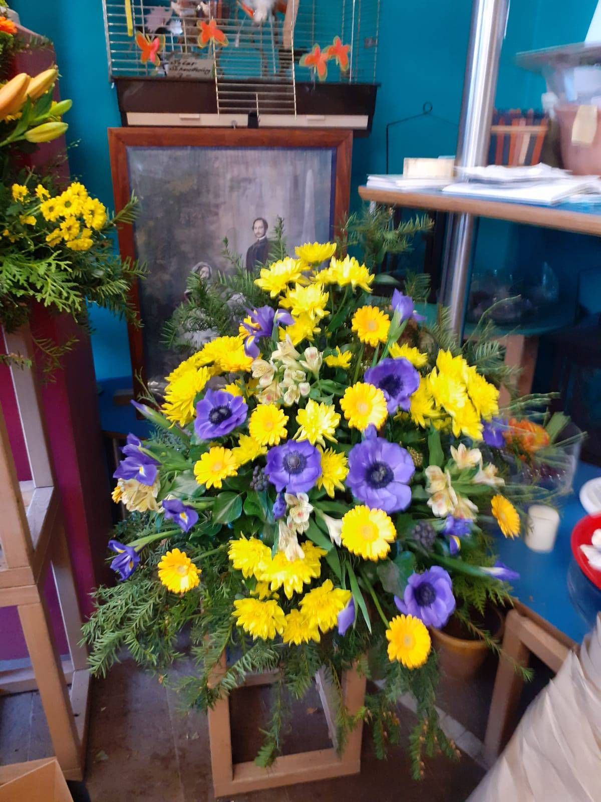 Blumenarrangement mit gelben und violetten Blumen vor einem gerahmten Foto.