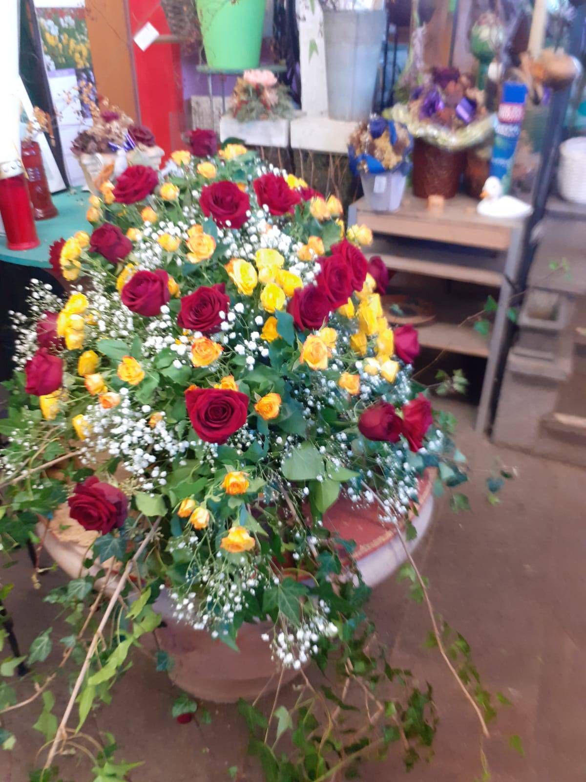 Großes Blumenarrangement mit roten und gelben Rosen, Schleierkraut und grünem Laub in einem braunen Topf.