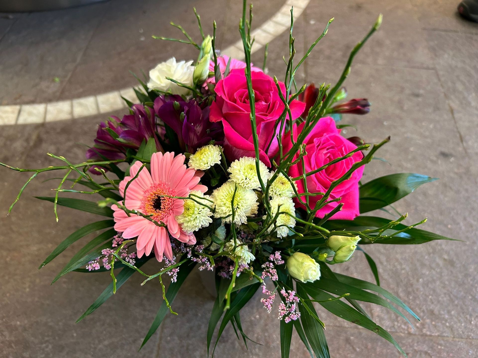 Nahaufnahme eines Straußes aus rosa und weißen Rosen mit grünem Füllmaterial, der auf einer Holzoberfläche steht.