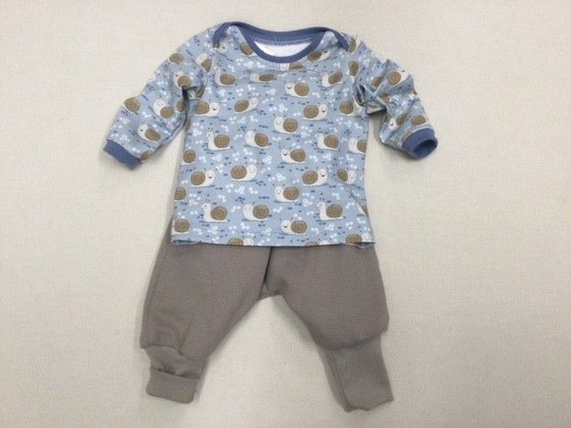 Baby-Outfit: blaues Langarmshirt mit Schneckenmuster und graue Hose, auf einer weißen Fläche liegend.